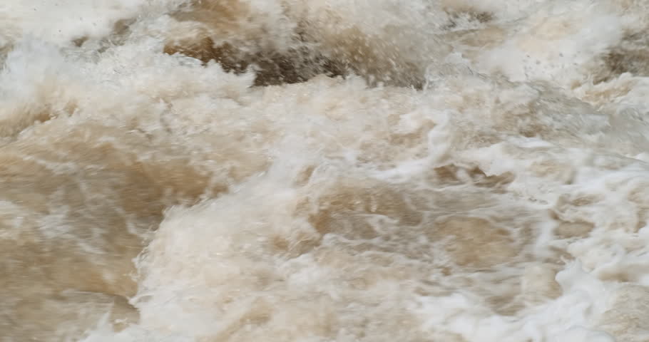 Brown fast mountain river water flowing, close up. Strong river flow in spring. Rapid muddy flood motion. Waterfall splashing. Dirty river with yellow water in flooding period during heavy rains. 4k