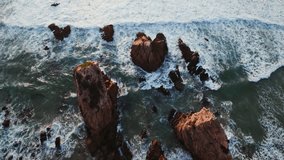 Top view of the foaming sea waves washing the coastal rocks, drone video
