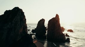 Sharp peaks of rocks on the seashore washed by sea waves. Drone video at sunset