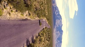 Car driving along asphalt highway road passing desert. Road trip to Death Valley. Top view of a yellow car driving on a road in the middle of the desert. Aerial vertical, vertical video background.
