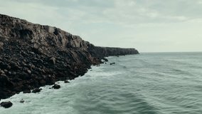 A rocky cliff on the seashore. The sea waves are beating against the rocks. Drone video