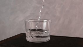 Clean drinking water pours into a transparent glass, forming air bubbles. Slow motion video.