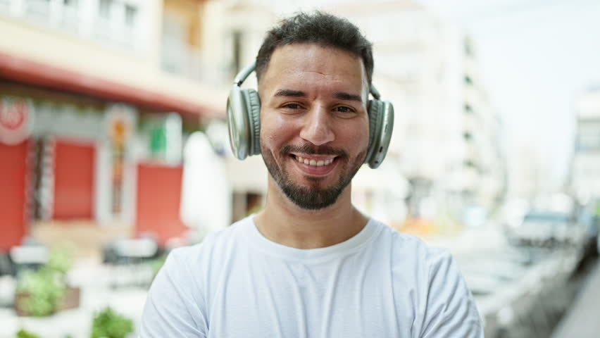 Young arab man listening to music standing with arms crossed gesture at coffee shop terrace