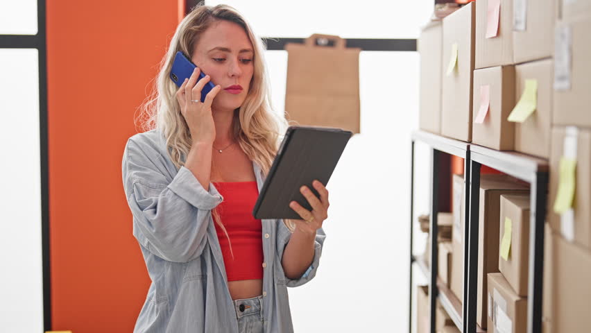 Young blonde woman ecommerce business worker talking on smartphone using touchpad checking at office