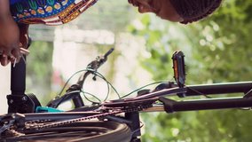 Vertical video Dedicated multiracial pair cautiously fastening bike chain and pedal for summer outdoor leisure cycling. Outdoorsy young couple thoroughly examining damages on bicycle wheel for
