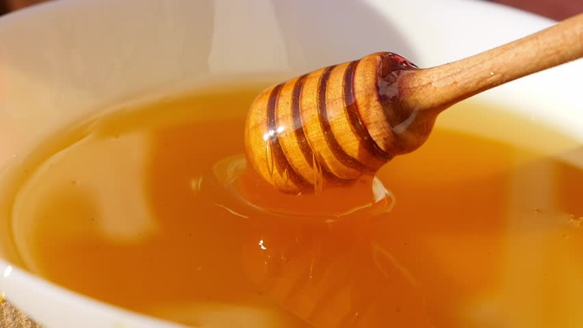 Honey is poured from a honey spoon into a plate. Freshly squeezed honey sparkles in the sun.