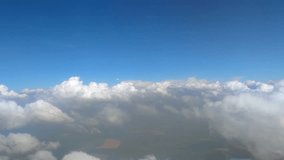 Side view through airplane window of white cumulus clouds flying in the sky avobe land. Real time handheld video. Beauty in nature theme.