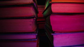 Towers of old books, slider macro footage in neon glowing room. Colorful light