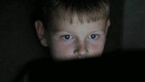 A boy watches a cartoon on a laptop or tablet in a dark room. The light from the screen plays on the face of a pretty boy about ten years old. - Powered by Shutterstock - Get 15% off with code: PIKWIZARD15