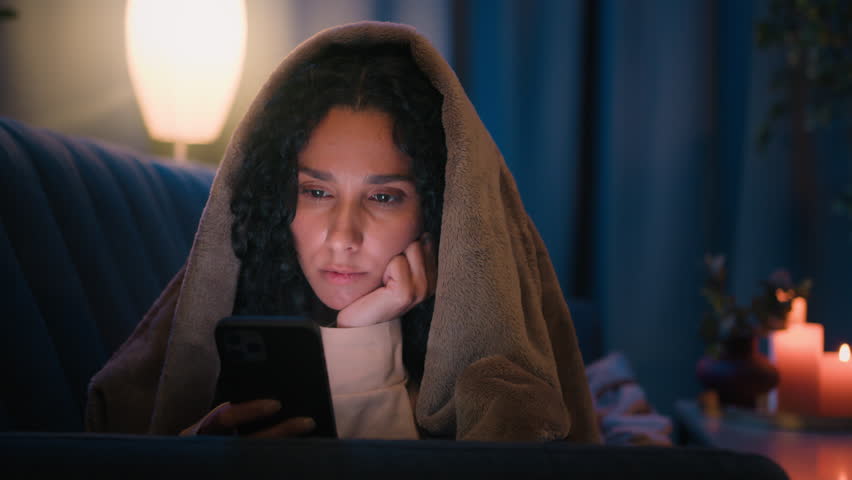 Tired exhausted sleepy Hispanic girl gadget addict lady chatting at nighttime fatigued internet social media addicted Latino woman insomnia at night at home under blanket boring mobile phone scrolling Royalty-Free Stock Footage #1107719555