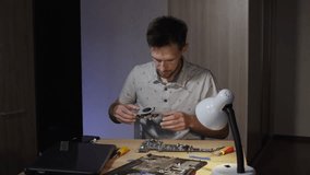 Computer hardware repairman attaches cooling system to circuit board while repairing laptop, static shot. Focused hispanic technical engineer sitting at desk in home office with lamp on. - Powered by Shutterstock - Get 15% off with code: PIKWIZARD15