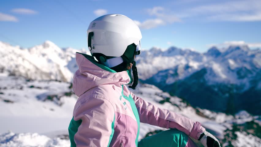 Back view woman in ski suits sitting on snow at top mountain and looking in distance. Skier resting on top mountain. Snowboarder sitting with snowboard. Enjoy beautiful winter landscape. Ski resort. Royalty-Free Stock Footage #1107722211