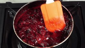 Blackberry jam is cooking in a saucepan and stirring with a silicone spatula in macro. Blackberries for marketing videos or promotions for restaurants, cafes and food video