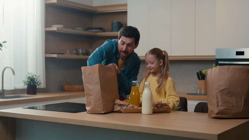 Happy family at kitchen home unpacking bag shopping purchase goods with milk bottle juice bread father dad give orange fruit vitamin to little daughter child kid girl food delivery service nutrition Royalty-Free Stock Footage #1107723967