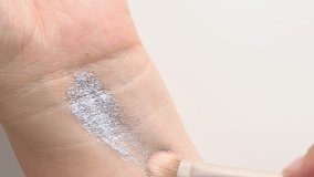 Brush gains silver gray glitter pigment on pile to be used in make-up. Artist working with eyeshadows. Decorative cosmetics. Close up shot of woman applying glitter on hand skin.  - Powered by Shutterstock - Get 15% off with code: PIKWIZARD15