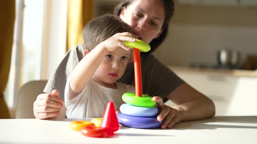 Happy family.Mom and son are play at table.Nanny in kindergarten teaching child.Mom teaches kid to value colored cubes.Babysitter deals with child Education in kindergarten.Baby with sitting at table Royalty-Free Stock Footage #1107729025