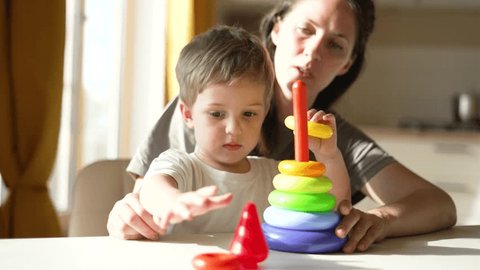Happy family.Mom and son are play at table.Nanny in kindergarten teaching child.Mom teaches kid to value colored cubes.Babysitter deals with child Education in kindergarten.Baby with sitting at table : vidéo de stock