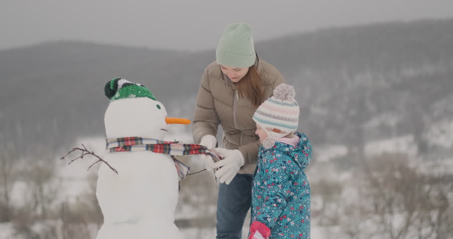 Little girl and mom walk outside on winter and make big snowmen. Happy winter holidays and family day
