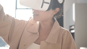 Beautiful young girl wearing virtual reality headset. Augmented Reality. Happy cute female touch something using modern 3D vr glasses indoors. Woman playing using VR goggles at home office. Sunny day