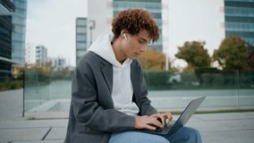 Young freelancer working computer at street closeup. Curly guy chatting social media at laptop outdoors. Calm blogger creating content at digital device. Hipster sitting at modern buildings district - Powered by Shutterstock - Get 15% off with code: PIKWIZARD15