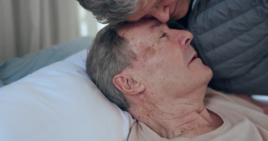 Love, face and senior people, sick patient or man ill from cancer in a hospice for healthcare, medical disease on hospital bed. Forehead touch, support care and elderly person with infection or virus