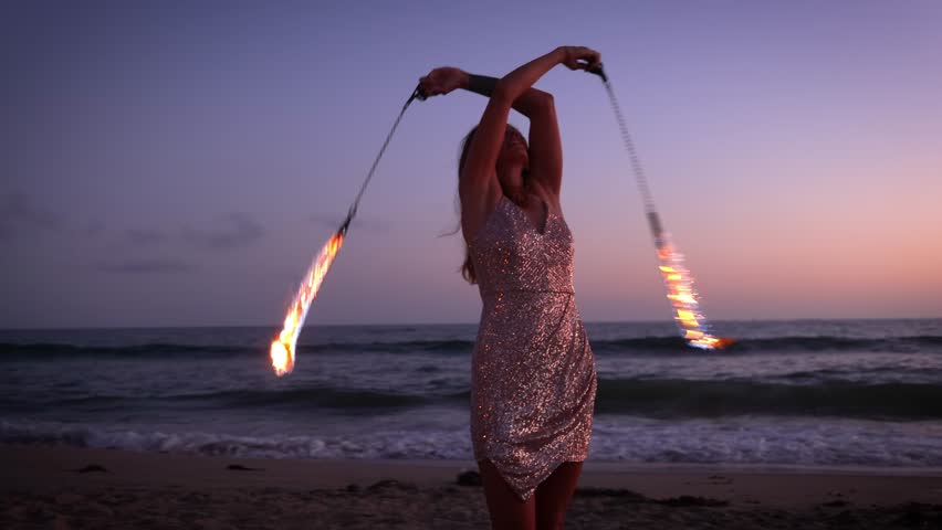 Attractive woman fire dancer spinning flames at the beach. Slow Motion.