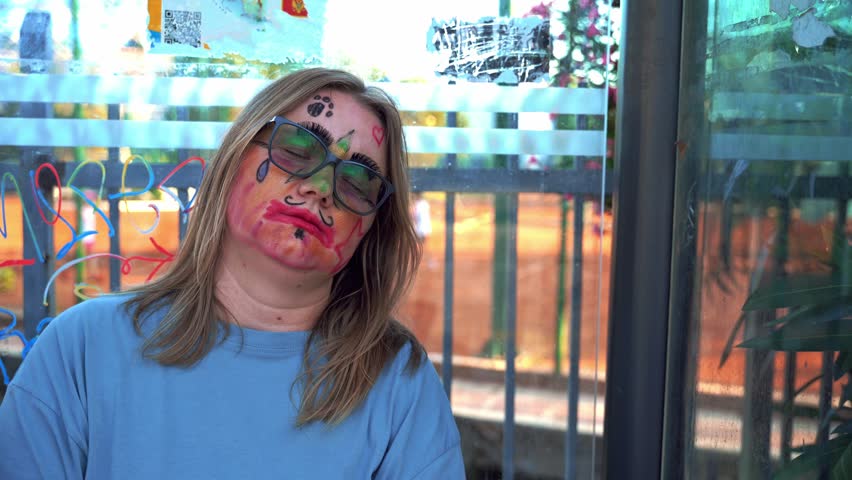 Woman with abstract makeup, painted face is sleeping at bus stop, car are reflected in window Contemporary art, social experiment street performance Tired children animator after shift April Fools Day