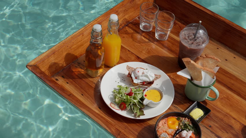 From a captivating top view, a floating egg benedict breakfast is set against a sunny backdrop. The poached egg, hollandaise sauce, and crispy bacon create a tantalizing visual feast Royalty-Free Stock Footage #1107740969