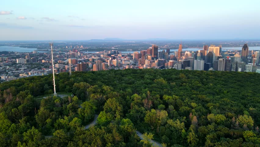 Aerial shot drone flies over Mount Royal toward downtown Montreal at sunset