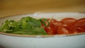 The girl puts green arugula in a plate with tomatoes