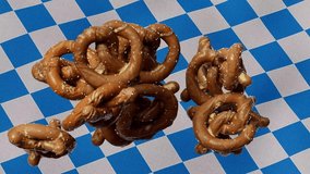 3D animated video of falling pretzels on the background of fabric pattern of the Bavarian flag Octoberfest. 4K 