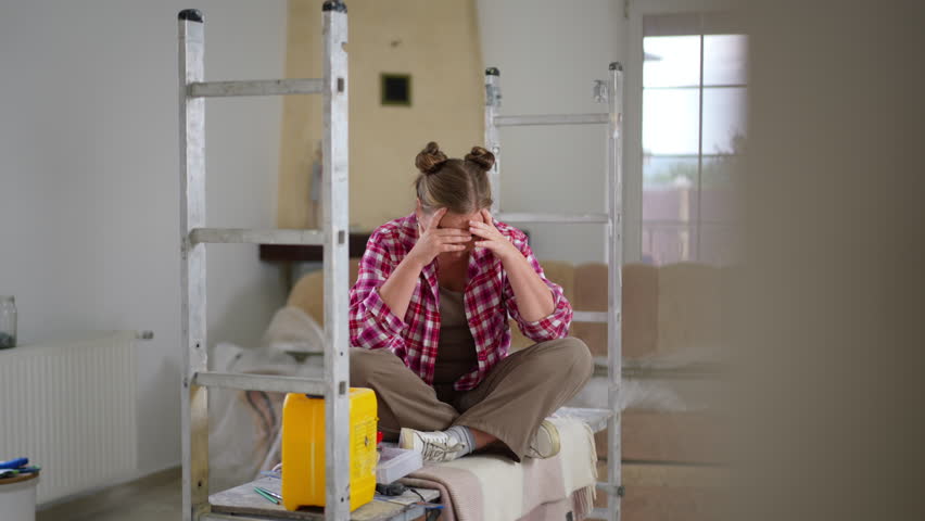 Wide shot stressed sad woman holding head in hands sitting in new house under repair. Overwhelmed Caucasian plus-size lady thinking looking around in slow motion | Shutterstock HD Video #1107746581