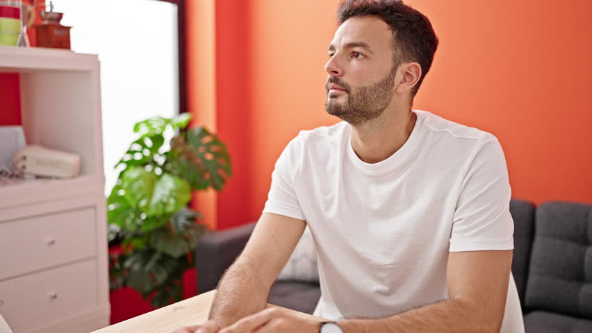 Young hispanic man sitting on table with serious expression at dinning room