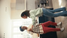 Vertical video of mature mother with teenage daughter at home in kitchen having fun dancing together - shot in slow motion