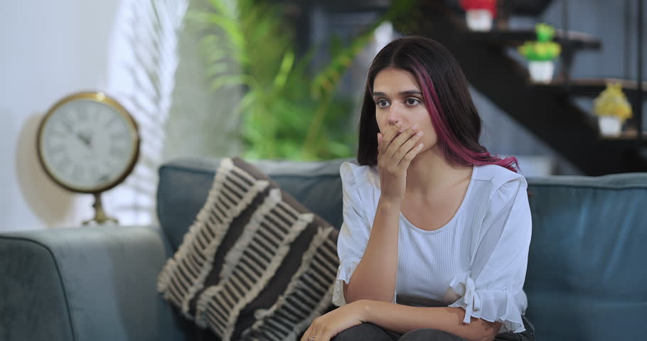 Indian Unhappy female sitting on sofa couch watching shocked bad news on TV at indoor house. Beautiful scared sad woman feeling panic suffer stress thinking negative hitting thigh with hand at home Royalty-Free Stock Footage #1107752511