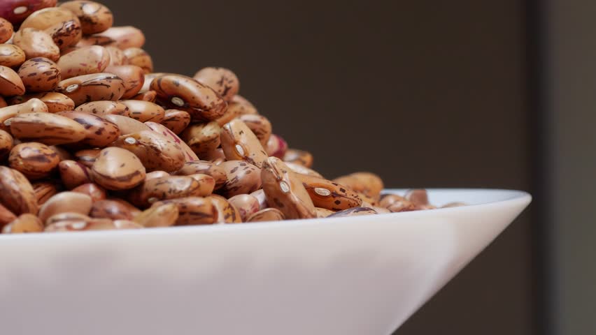 A bowl of beans with black spots on a table, set against a black background
