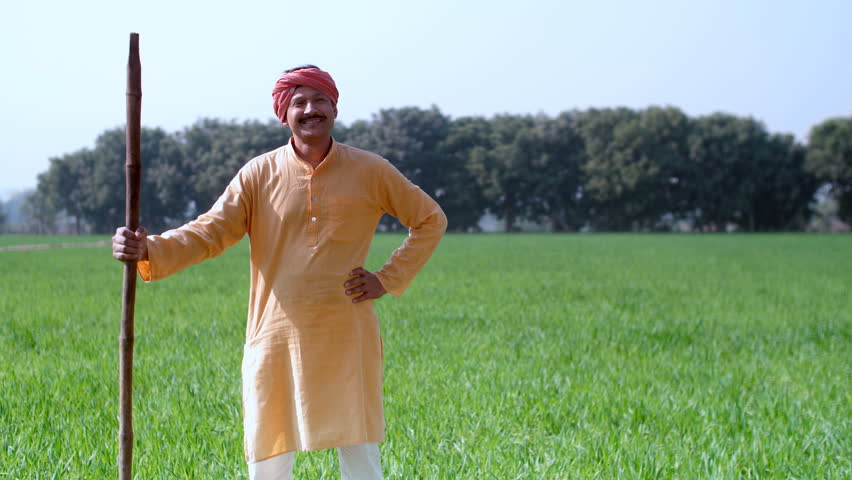 Portrait of a confident, smiling farmer standing with a stick in his field - village lifestyle. A happy labourer of an Indian village holds a stick on his shoulder and posing Royalty-Free Stock Footage #1107754311
