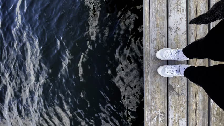 the girl comes to the edge of the wooden bridge by the pond, the water is dark blue, the woman stands at the edge of the bridge by the water