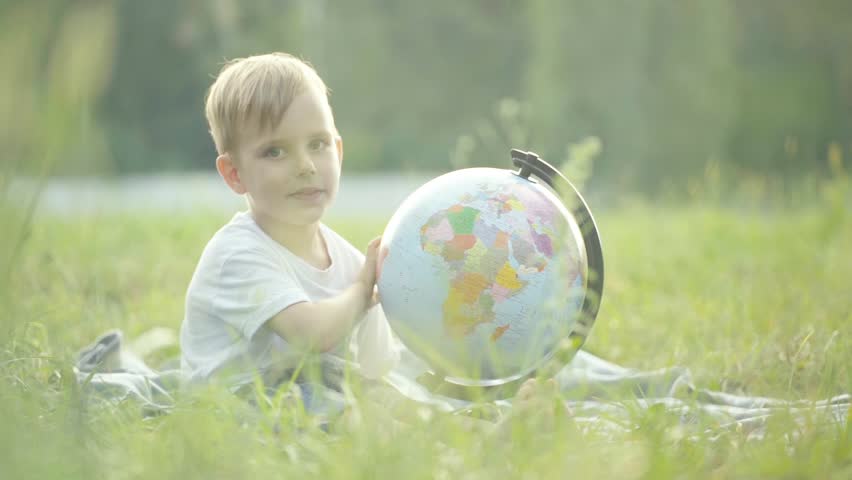 A little boy hugs a globe and smiles. Slow motion. Sunset.