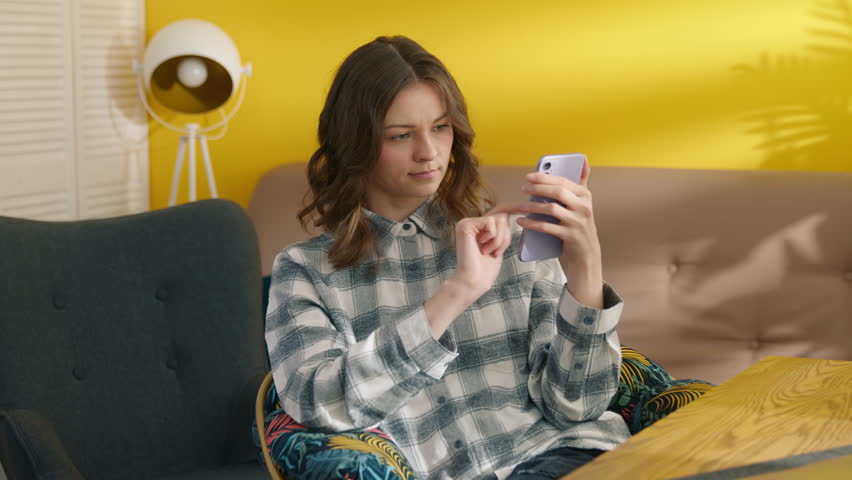 Serious girl browsing internet on smartphone. Collage student using cellphone at home after online lessons. Focused woman sitting at table in room. Pretty lady using mobile phone, 4k footage