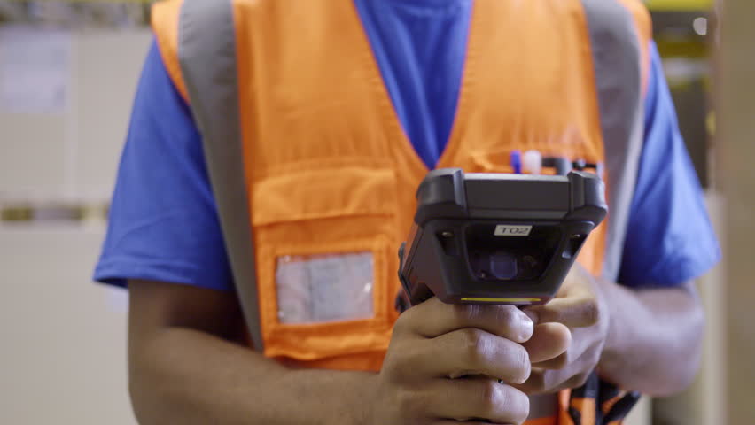 Warehouse worker holding barcode scanner and using management system close up. Storehouse employee in safety vest holding handheld bar code reader device closeup Royalty-Free Stock Footage #1107775579
