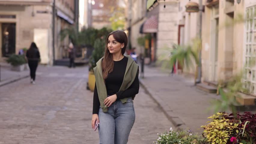 Casual walk, Street photography, Leisurely stroll. While strolling down street, gorgeous young woman clicks photos using mobile device.