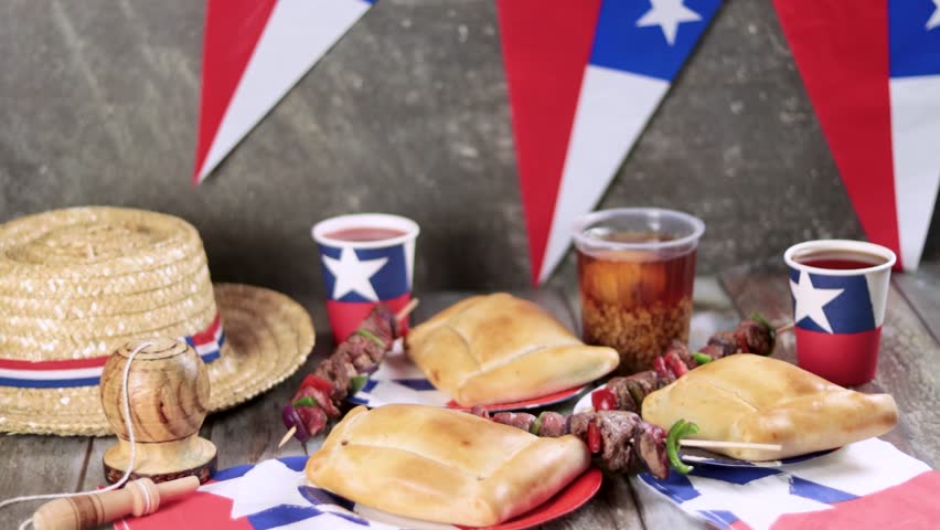 Fiestas Patrias Chile September 18, Independence Day. Empanadas, Anticuchos, mote con huesillo, chicha or wine, Sombrero, huaso, chupallas, straw and emboque, on a wooden table with flag and colorful Royalty-Free Stock Footage #1107786555