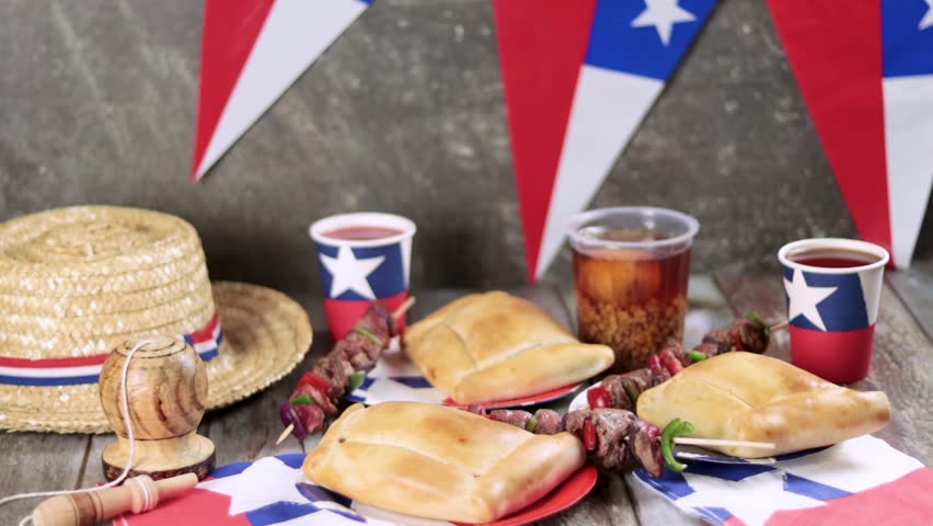 Fiestas Patrias Chile September 18, Independence Day. Empanadas, Anticuchos, mote con huesillo, chicha or wine, Sombrero, huaso, chupallas, straw and emboque, on a wooden table with flag and colorful 