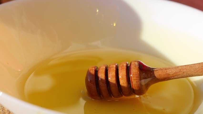 Honey is poured from a honey spoon into a plate. Freshly squeezed honey sparkles in the sun.