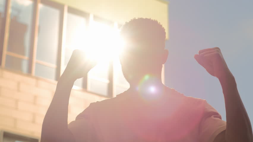 Happy winner successful African American university student guy man male outdoors in city education success good results win achieve winning in sun sunshine rise hands champion victory achievement Royalty-Free Stock Footage #1107803307