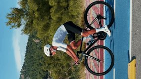 Man in white helmet and shoes riding road bicycle on cycle path. Vertical video. Professional road cyclist cycling outdoors. Fit athletic male athlete training on bike, doing intense cardio exercises