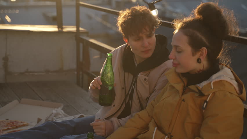 4k Two lesbian women in love drink and sit on roof in city spbd. Young lgbt couple drinking beer and looking with smiles, posing and sitting on terrace outdoors. Happy homosexual people or family hang | Shutterstock HD Video #1107804113