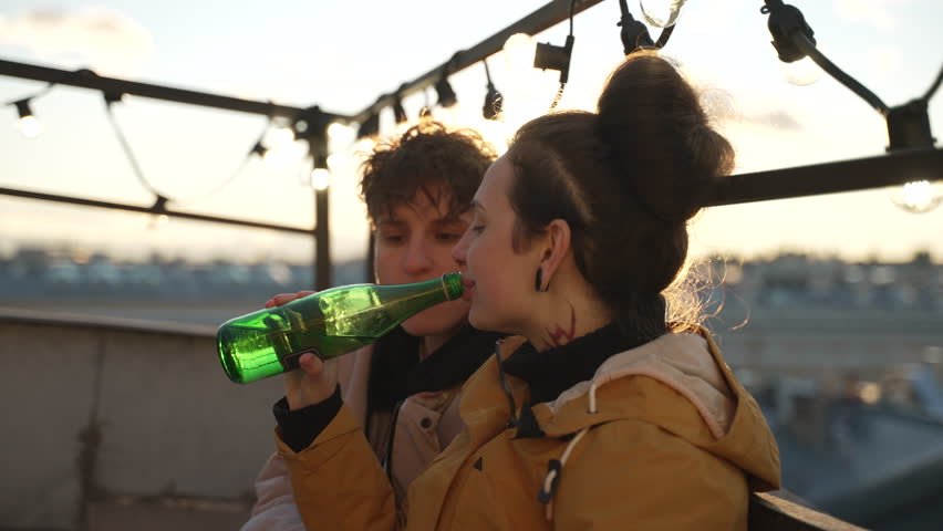 4k Lesbian women drink and talk on rooftop in city spbd. Young lgbt couple talking and looking with smiles, drinking beer and sitting on roof of building outdoors. Two equality girlfriends have good | Shutterstock HD Video #1107804115