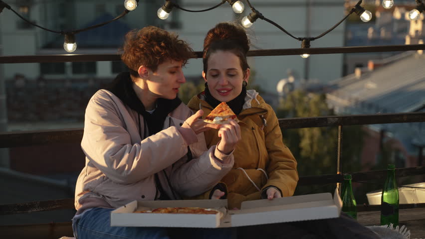 4k Female homosexual couple eats and drinks on rooftop in city spbd. Young lesbian women eating pizza and drinking beer, looking with smiles and posing on roof in town. Beautiful lgbt partners or | Shutterstock HD Video #1107804117
